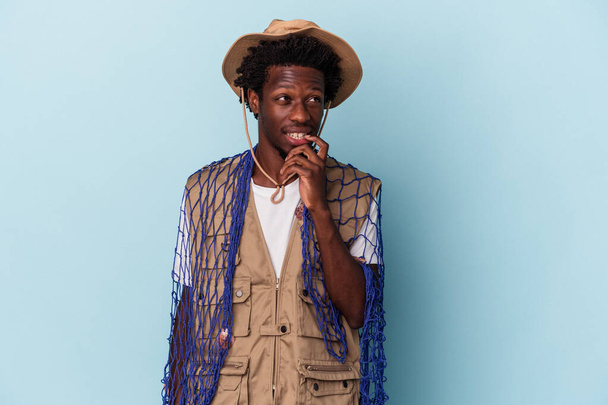 Young african american fisherman holding a net isolated on blue background relaxed thinking about something looking at a copy space. - Фото, изображение