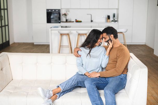 Gentle and lovely couple in love sitting in embrace on the comfortable sofa at home, looking to each other tenderly. Concept of support and caring - Photo, image