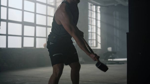 Sportsman frapper pneu avec un marteau dans la salle de gym. Homme faisant de l'exercice avec un marteau - Photo, image