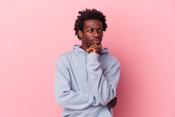 Νεαρός Αφροαμερικάνος απομονωμένος σε ροζ φόντο χαλαρός σκεπτόμενος κάτι κοιτάζοντας ένα χώρο αντιγραφής. - Φωτογραφία, εικόνα