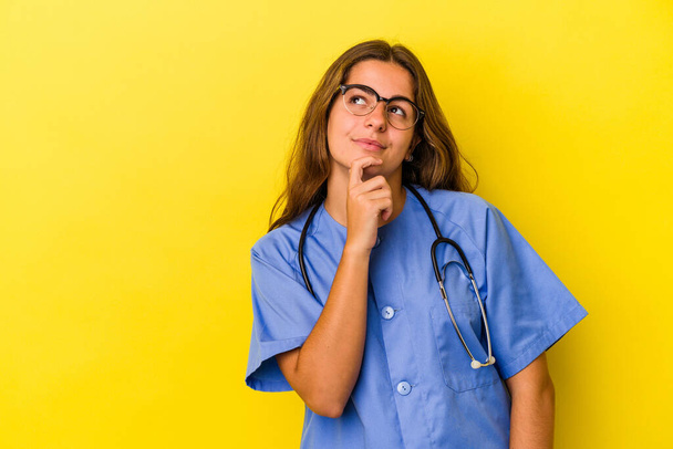 Mladá zdravotní sestra žena izolované na žlutém pozadí při pohledu bokem s pochybné a skeptický výraz. - Fotografie, Obrázek