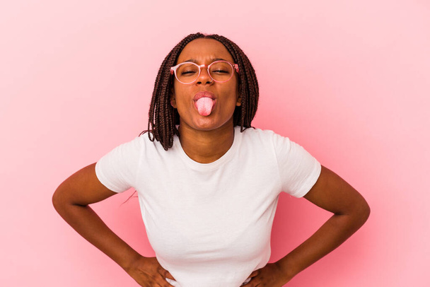 Joven afroamericana americana aislada sobre fondo rosa divertida y amigable sobresaliendo lengua. - Foto, Imagen