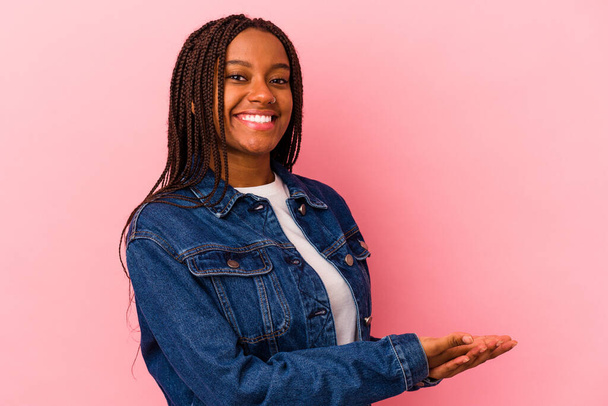 Joven mujer afroamericana aislada sobre fondo rosa sosteniendo un espacio de copia en una palma. - Foto, Imagen