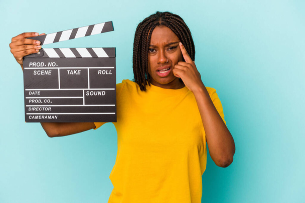 jonge afrikaanse amerikaanse vrouw houden een klapbord geïsoleerd op blauwe achtergrond tonen een teleurstelling gebaar met wijsvinger. - Foto, afbeelding