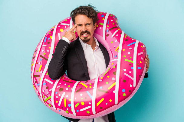 Young business man with inflatable donut isolated on blue background showing a disappointment gesture with forefinger. - Foto, Bild