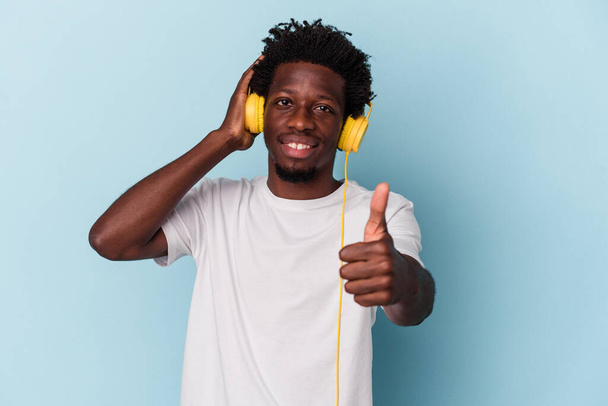 Nuori afrikkalainen amerikkalainen mies kuuntelee musiikkia, joka on eristetty sinisellä taustalla, koskettaa takaraivoa, ajattelee ja tekee valinnan.. - Valokuva, kuva