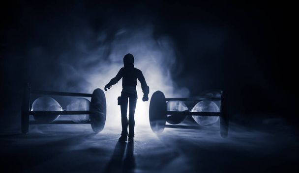 Concepto de tiempo. Silueta de un hombre parado entre clepsidras con humo y luces sobre un fondo oscuro. Imagen surrealista decorada - Foto, imagen