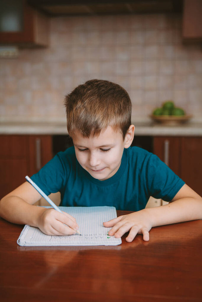Cute child writing letters in notebook sitting by table - Photo, Image