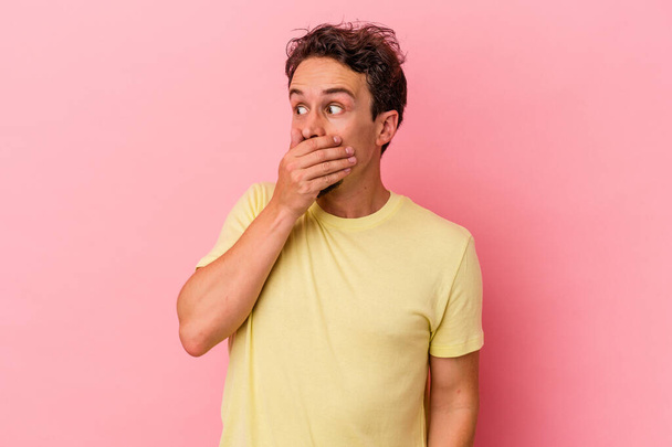 Young caucasian man isolated on pink background thoughtful looking to a copy space covering mouth with hand. - Фото, зображення