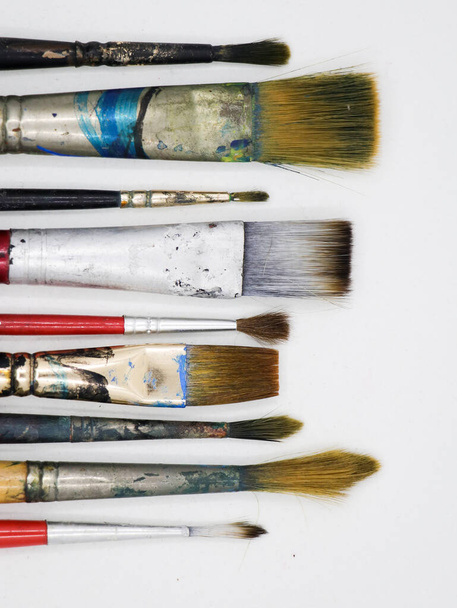 vertikální záběr skupiny dřevěných umělců malovat štětce různých tvarů a velikostí, s barevnými skvrnami uspořádány rovnoběžně s sebou izolované v bílém pozadí - Fotografie, Obrázek