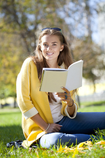 Beautiful schoolgirl sitting in autumn park and reading a book - Φωτογραφία, εικόνα
