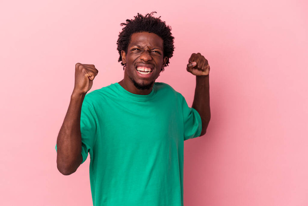 Молодой африканский американец, изолированный на розовом фоне, поднимающий кулак после победы, концепция победителя. - Фото, изображение