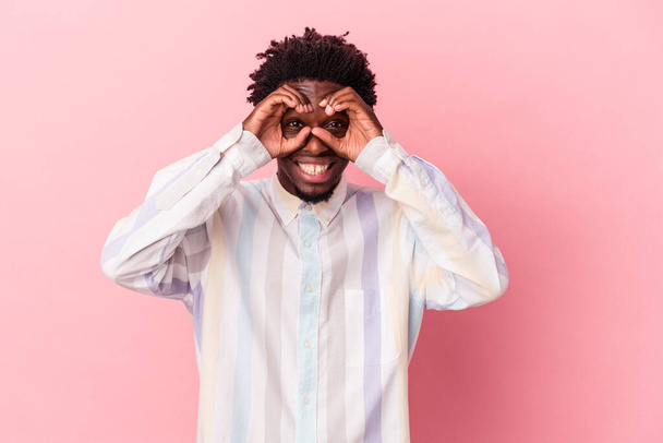 Young african american man isolated on pink background showing okay sign over eyes - 写真・画像