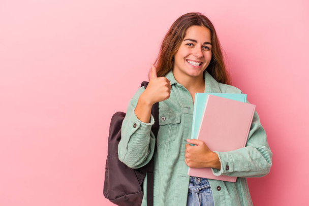 Mladá běloška studentka drží knihy izolované na růžovém pozadí s úsměvem a zvednutím palce nahoru - Fotografie, Obrázek
