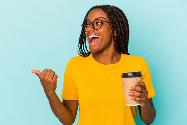 Młoda Afroamerykanka trzymająca kawę na niebieskim tle odizolowaną kciukiem, śmiejąca się i beztroska. - Zdjęcie, obraz
