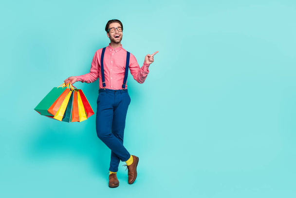 Photo of impressed cute guy dressed pink shirt spectacles bags pointing finger empty space isolated turquoise color background - Foto, afbeelding