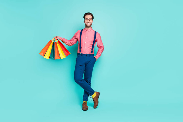 Photo of funky sweet young gentleman wear pink shirt glasses yellow socks holding colorful bargains smiling isolated teal color background - Foto, Bild