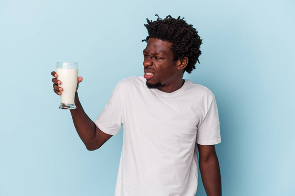 Молодой африканский американец держит стакан молока изолирован на синем фоне - Фото, изображение