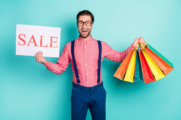 Photo of young man happy positive smile hold bags shopper hold banner sale isolated over turquoise color background - Φωτογραφία, εικόνα