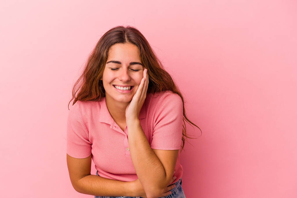 Young caucasian woman isolated on pink background  laughs happily and has fun keeping hands on stomach. - 写真・画像
