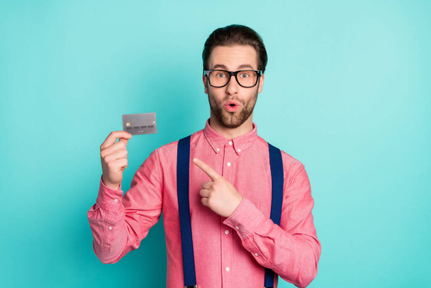 Photo of impressed cute young guy dressed pink shirt spectacles pointing finger credit card isolated turquoise color background - Φωτογραφία, εικόνα