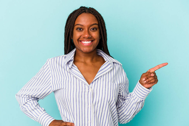Junge afrikanisch-amerikanische Frau isoliert auf blauem Hintergrund lächelt fröhlich und zeigt mit dem Zeigefinger weg. - Foto, Bild
