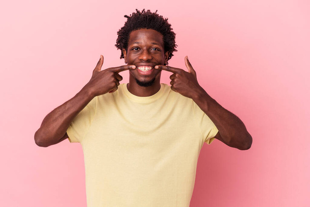 Young african american man isolated on pink background smiles, pointing fingers at mouth. - Photo, Image
