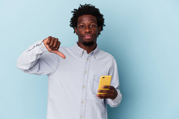 Junger afrikanisch-amerikanischer Mann, der sein Handy isoliert auf blauem Hintergrund hält und eine ablehnende Geste zeigt, Daumen nach unten. Konzept der Uneinigkeit. - Foto, Bild