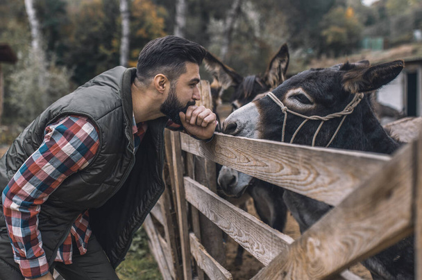 Dark-haired farmaer standing near the stall with donkeys - Foto, imagen