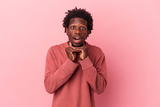 Fiatal afro-amerikai férfi elszigetelt rózsaszín háttér imádkozik a szerencséért, meglepett és nyitott száj keres elöl. - Fotó, kép