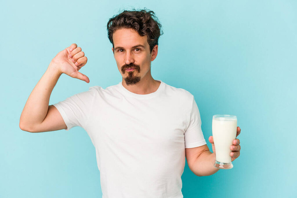 Jeune homme caucasien tenant un verre de lait isolé sur fond bleu se sent fier et confiant, exemple à suivre. - Photo, image