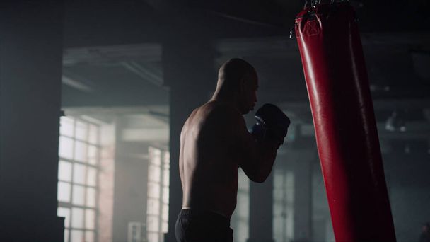 Boxer batendo saco de soco durante o treino intenso. Homem praticando kickboxing no ginásio - Foto, Imagem