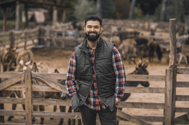 A farmer in the black vest and a plaid shirt standing near the cattle-pen - Φωτογραφία, εικόνα