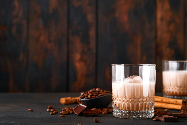 Glass of Irish cream baileys liqueur with roasted coffee beans, cinnamon and chocolate on dark wood background table. Selective focus. - Foto, Bild
