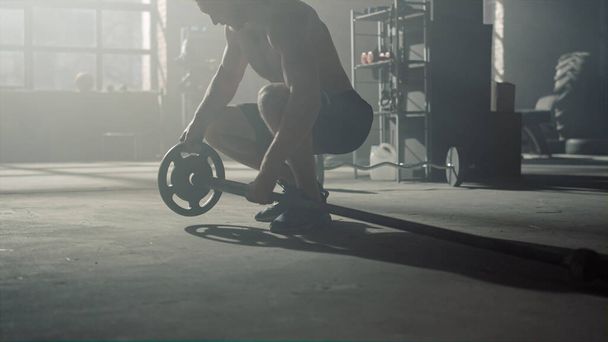 Мужчина ходит в кроссфитовом спортзале. Культурист готовит спортивный инвентарь для тренировок - Фото, изображение
