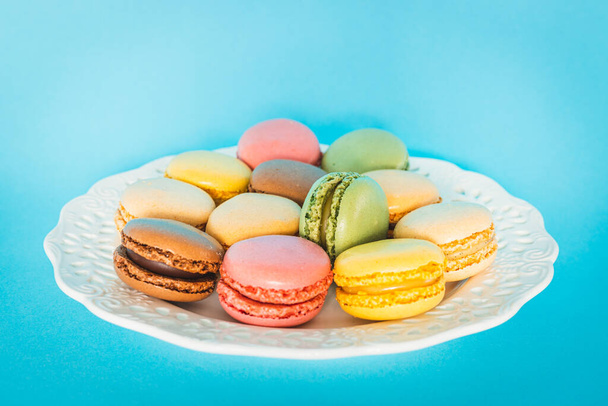 Πολύχρωμα Macaroons, Delicious Γαλλικά μπισκότα σερβίρονται σε ένα πιάτο σε ένα κομψό στυλ, Μπλε φόντο  - Φωτογραφία, εικόνα