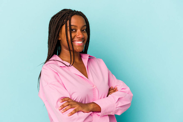Jonge Afro-Amerikaanse vrouw geïsoleerd op blauwe achtergrond die zich zelfverzekerd voelt, kruisende armen met vastberadenheid. - Foto, afbeelding