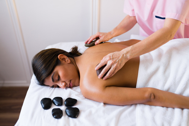 Atrakcyjna młoda kobieta korzystająca z relaksującego masażu gorącymi kamieniami na plecach  - Zdjęcie, obraz