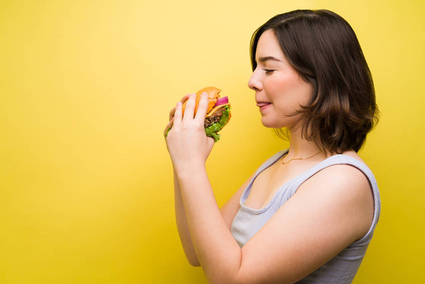 Lecker! Hungrige junge Frau hält einen leckeren Hamburger in der Hand und isst Mittagessen  - Foto, Bild