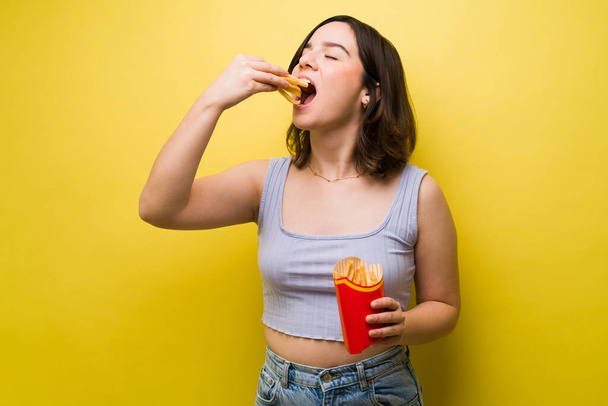 Ik hou van frietjes. Aantrekkelijke vrouw in de 20 eten heerlijke frietjes tegen een gele achtergrond - Foto, afbeelding
