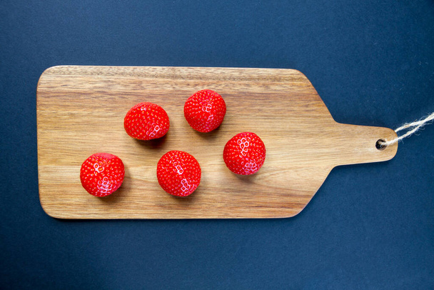 Strawberries on a wooden cutting board. Black background. Top view - 写真・画像