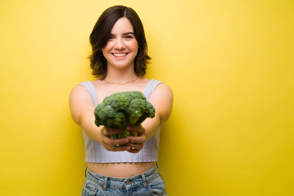 Portret van een gelukkige vrouw in de 20 met een gezond dieet dat broccoli eet  - Foto, afbeelding