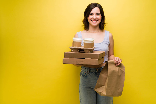 Emocionada jovencita saliendo a comprar comida para llevar. Hermosa mujer sosteniendo cajas de pizza y café para llevar - Foto, imagen