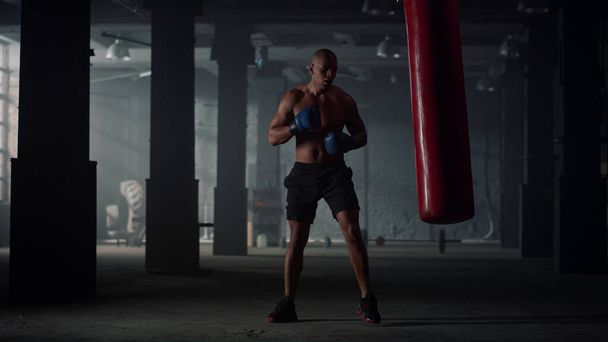 Hombre golpeando saco de boxeo durante el entrenamiento intenso. Boxeador masculino practicando kickboxing - Foto, Imagen