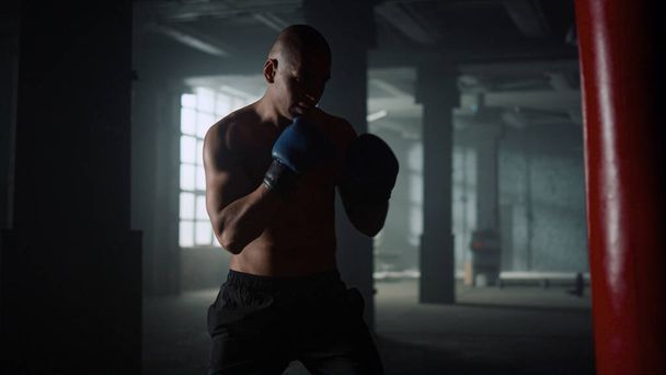 Boxer pratique coups de pied sur sac de boxe dans la salle de gym. Guy sac de sport de boxe en gants - Photo, image