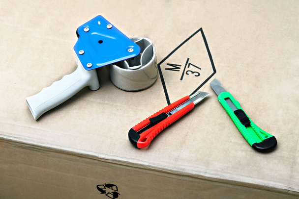 Confezionamento Tape Gun Dispenser e coltelli fissi sdraiati su scatola di cartone
 - Foto, immagini
