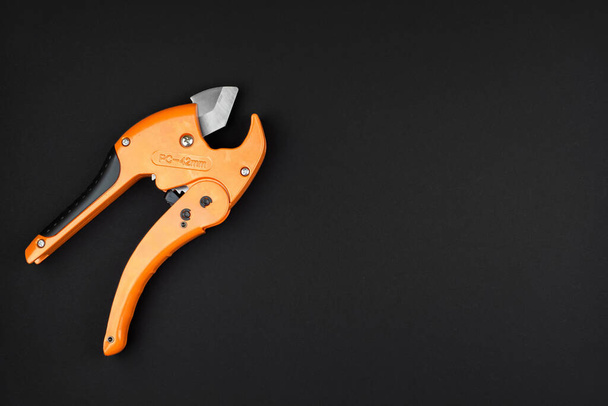 orange scissors for cutting propylene pipes on a black background - Foto, afbeelding