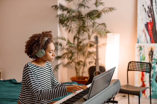 Kobieta muzyk w słuchawkach gra syntezator w domu - Zdjęcie, obraz