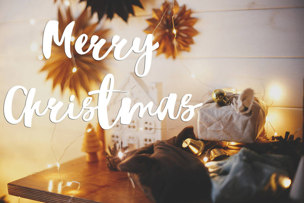 Καλά Χριστούγεννα κείμενο για το κομψό φιλικά προς το περιβάλλον δώρα Χριστουγέννων, μικρό σπίτι, δέντρα, αστέρια και τα Χριστούγεννα χρυσά φώτα bokeh. Η κάρτα χαιρετισμού της σεζόν. Χειρόγραφο σημάδι. Καλές γιορτές.! - Φωτογραφία, εικόνα