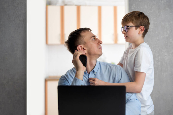 Tienerzoon leidt zijn vader af van zijn werk. Jonge zakenman probeert thuis te werken met kinderen - Foto, afbeelding